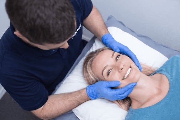 TMJ treatment physiotherapy with jaw support for female patient during clinic assessment