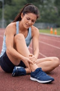 Female runner with a suspected common sports injury holding her ankle on a running track